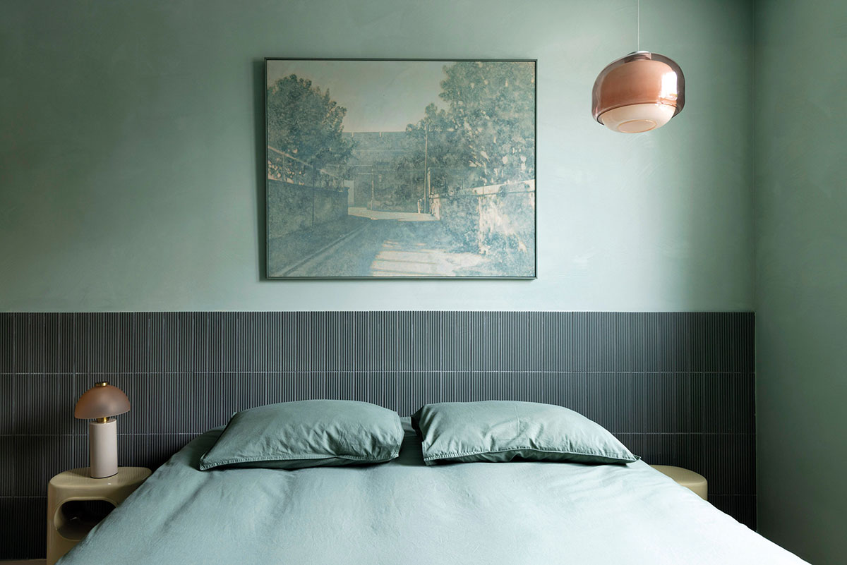 Chambre monochrome verte avec tête de lit en carreaux, tableau de paysage et suspension en verre rosé