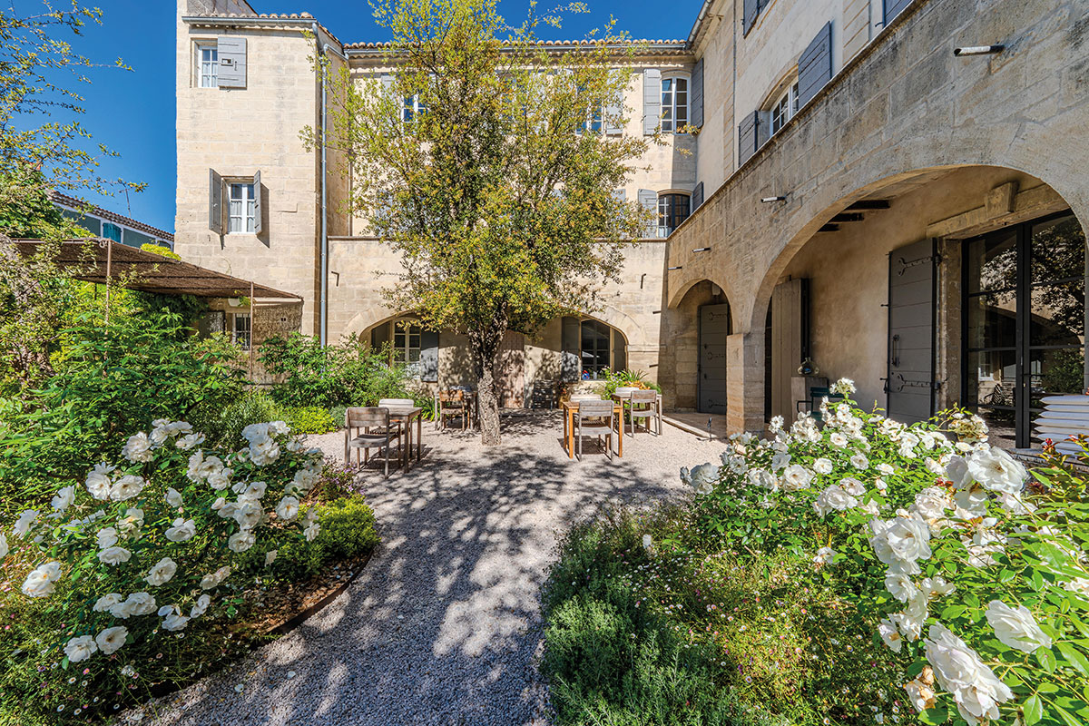 Cour intérieure de la demeure d’Uzès, gravier clair, rosiers blancs et façade en pierre aux volets gris