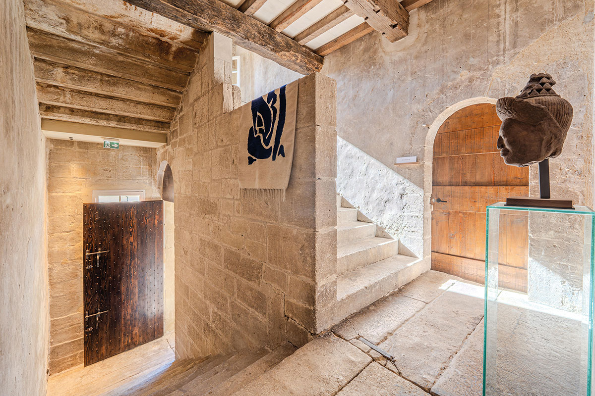 Escalier en pierre de la demeure, porte en bois cloutée, porte voûtée et tête sculptée sous vitrine en verre
