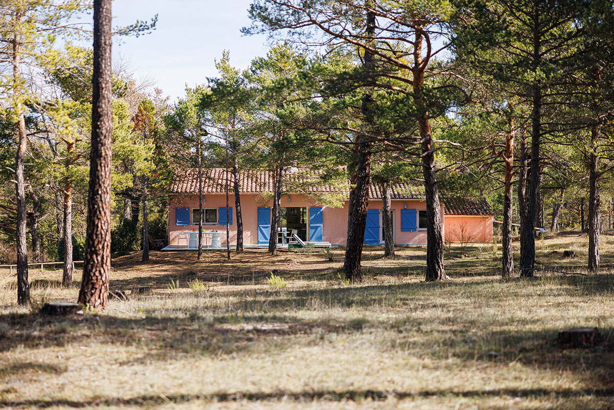 Façade rose aux volets bleus de la maison, entourée de pins dans le Haut-Var