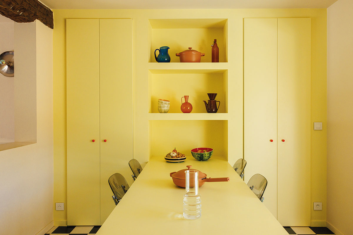 Salle à manger jaune citron avec placards, niches de rangement, table sur pied conique et chaises transparentes