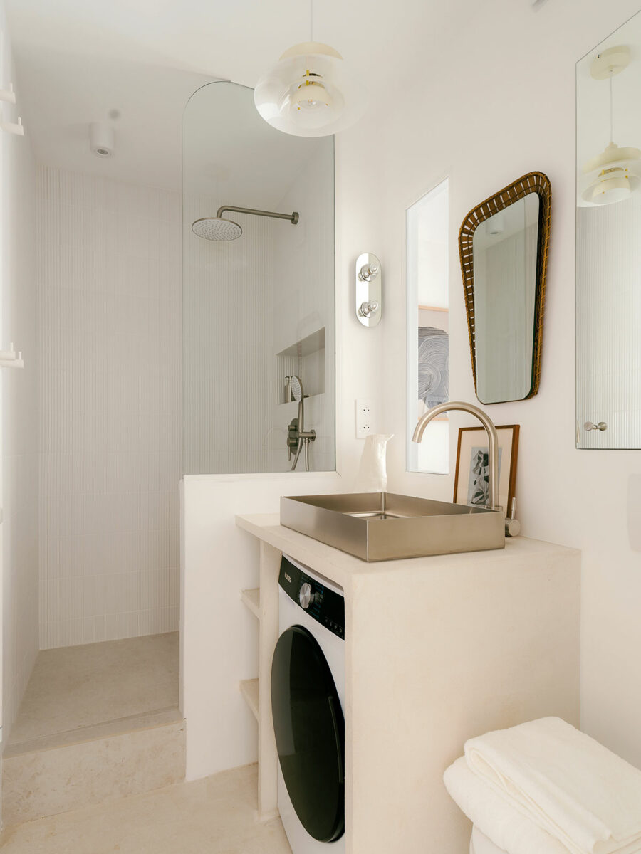 Salle d’eau aux murs en carrelage en relief blanc, douche ouverte, vasque en inox brossé et miroir au cadre tressé