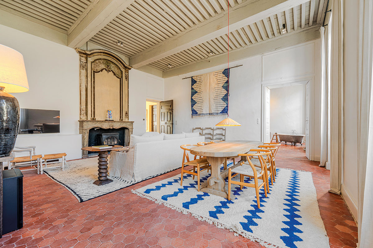 Salon au sol en carreaux de terre cuite hexagonaux, cheminée ancienne, table en bois et tapis blanc à zigzags bleus